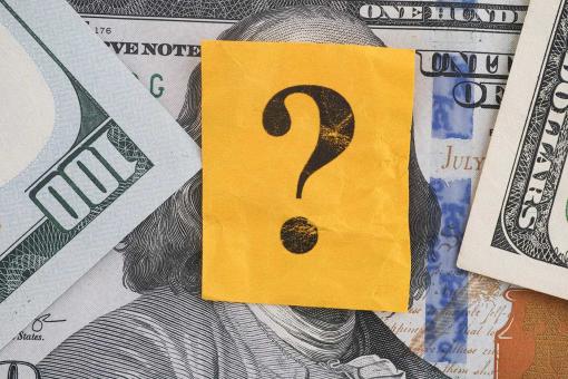 A question mark lying on some dollar bills