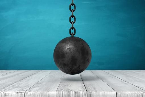 Black wrecking ball hanging above wooden surface.
