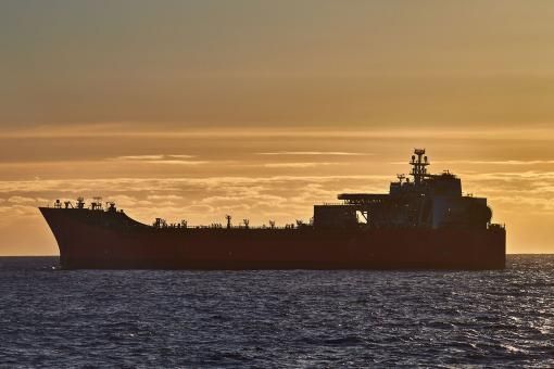 Beautiful ocean sunset, with golden sky, dark blue sea and silhouette of ship, oil tanker on the horizon.
