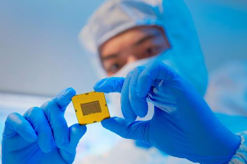 Male design engineer in sterile coverall holds microchip with gloves and examines it - ultra modern electronic manufacturing factory